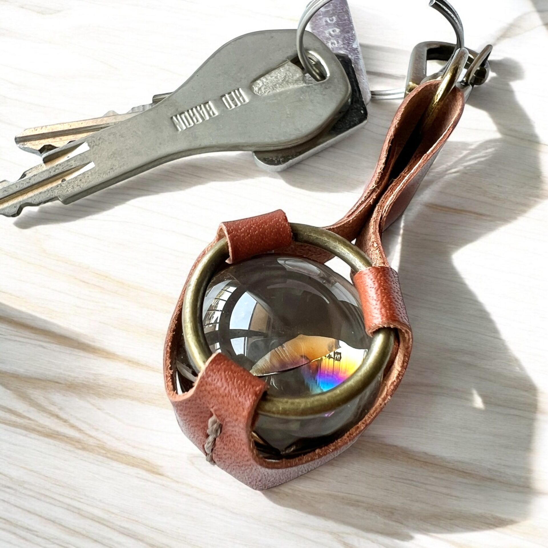 虹色の輝きが美しいアイリスクォーツ（虹入り水晶）を、手縫いレザーで丁寧に包んだハンドメイドキーホルダーです。 太陽光や室内の光を受けて、天然石の中にきらりと現れる虹は、忙しい毎日にふと「ときめき」と「癒し」をもたらしてくれます。 シンプルなバッグやお部屋のインテリアはもちろん、車内チャームやサンキャッチャーとしても大活躍。 お守りとしてはもちろん、大切な人への贈り物にもぴったりです。